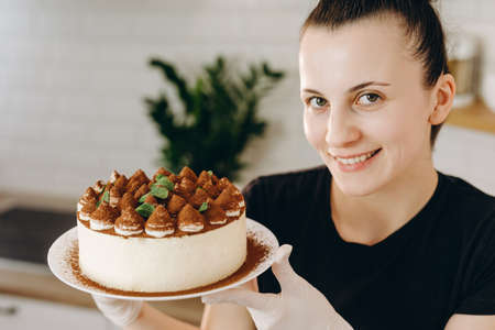 Attractive confectioner holding tiramisu cake on the kitchen.
