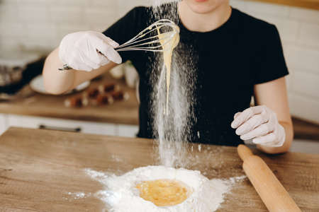 Baker s hands with plain flour well and eggs in preparation process for baking, cooking, pastry...