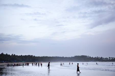 Palolem, India-September 1, 2012. Several tourists spend the last hours of the day enjoying the sea on the shore as the tide rises and the sky begins to sunsetのeditorial素材