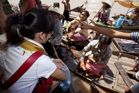 Chong Kneas, Cambodia-   Many tourists visit a floating village near Siem Reap  The villagers are coming up with their boats to tourists and they throw them candy and useless things thinking that help them with their charityのeditorial素材