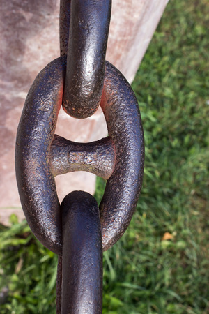 Detail of an old rusty chain with stone pillar on a green background. In the background is green grass.の写真素材