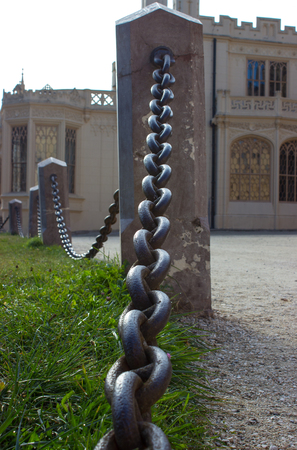 The gravel-covered walkway is separated from the lawn by a chain with stone pillar. In the background is the castle Lednice.のeditorial素材