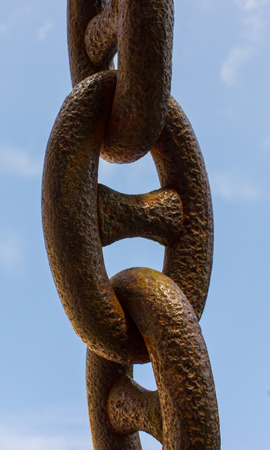 An old rusty chain on a blue background. In the background is blue sky with white clouds.の写真素材