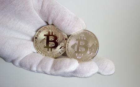 On hand in white glove are silver coins of a digital crypto currency - Bitcoin.