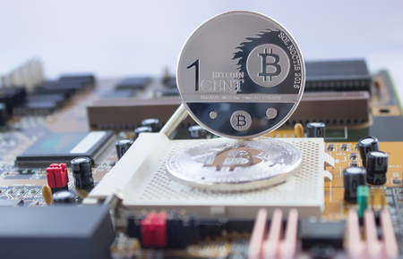 On a printed circuit motherboard are silver coins of a digital crypto  currency - bitcoin and one cent. One cent of the bitcoin stands on a lying bitcoin.の写真素材