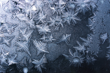 Ornaments on a frozen window on a black background in blue. Frozen water on the window creates...