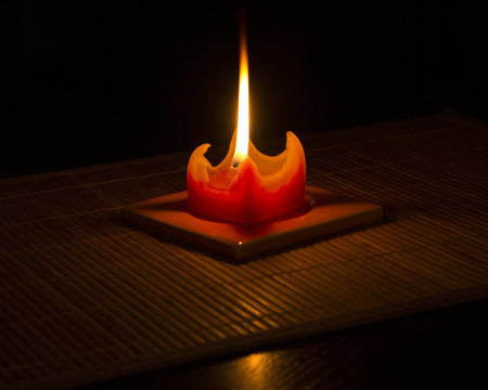 Red candle on bamboo mat with reflection in glossy table with black background.の写真素材
