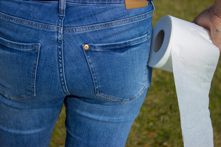 Woman bottom jeans toilet paper hand and grass in background