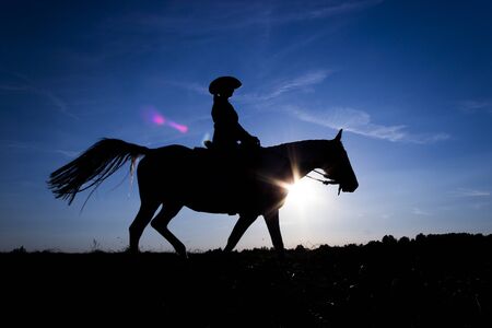Silhouette cowgirl riding on open plain in western at sunset in blueの写真素材