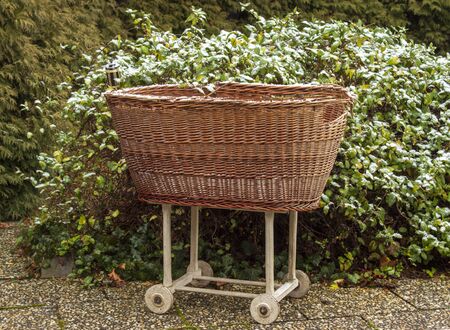 Old wicker basket for baby on wheels on the garden in winter.の写真素材