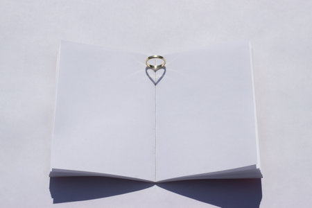 Summer wedding mockup. Blank wedding book on a white table. Wedding ring is placed on the book and the sunlight creates a heart-shaped shadow.の写真素材