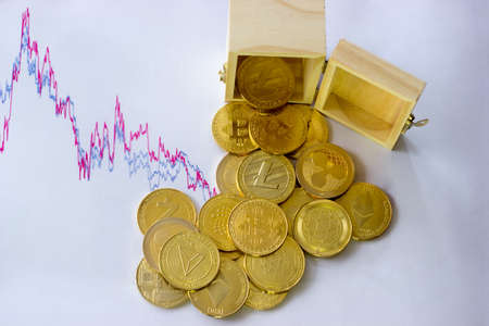 Cryptocurrencies emptied from a wooden box. In the background is a graph with a declining trend.の写真素材