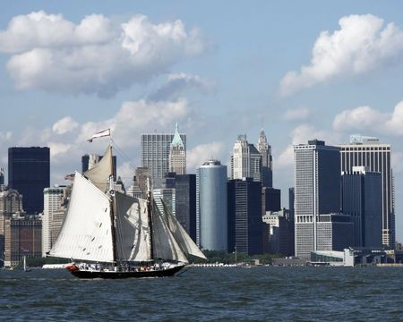 Schooner rigged sailboat in New York Harbor with Lower Manhattan in the background.