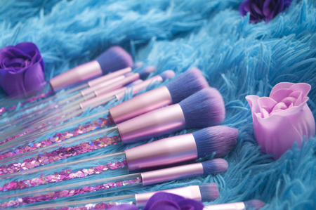 Set of makeup brushes with sparkles on pink, lilac and blue colored composed background.