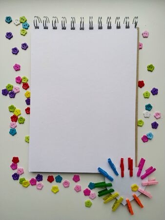 Notebook on the rings for drawing on a white background with multi-colored buttons in the shape of flowers and colorful clothespinsの写真素材
