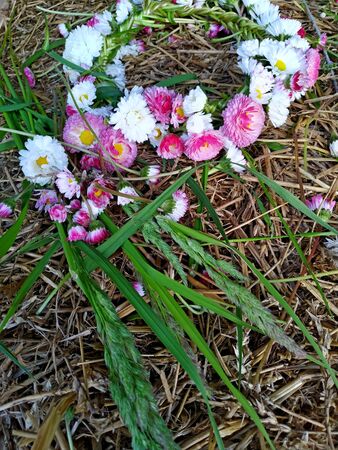 a wreath of white and pink daisies lies on a haystack next to freshly picked long grass. mobile...