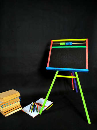 Small blackboard, color pencils and stack of books isolated on black background. Back to school.