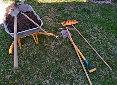 wheelbarrow with compost and orange tools to prepare the garden for planting. Orange garden tools on...