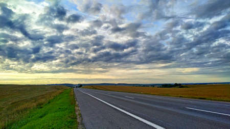 one truck drives on an empty highway between agricultural fields under a dawn sky with light cloudsの写真素材