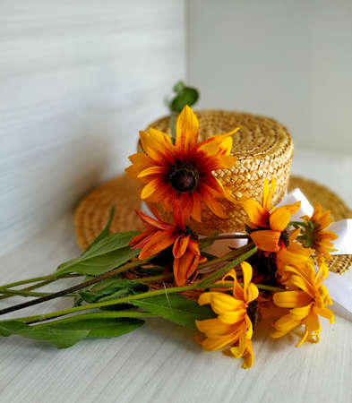 golden bicolor rudbeckia lies on a wicker straw hat on a light wood background. Selective focusの写真素材