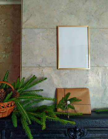 a christmas gift wrapped in craft paper and tied with linen thread on a mantelpiece next to fir branches in a wicker basket. Mock up over the fireplace with a christmas present and decorationの写真素材