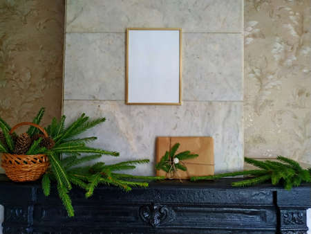 a christmas gift wrapped in craft paper and tied with linen thread on a mantelpiece next to fir branches in a wicker basket. Mock up over the fireplace with a christmas present and decorationの写真素材