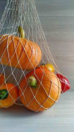 harvest time. Pumpkins and yellow and red peppers in a string bag on a light wood background.