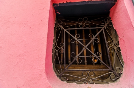 An old window on a pink wall in an old colonial building in La Candelaria neighborhood in Bogota, Colombiaの写真素材
