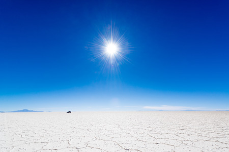 View of the sun over the Uyuni Salt Flats in Bolivia with an SUV in the background の写真素材