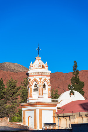 Spire of the cathedral in Tupiza, Bolivia with red hills in the backgroundの写真素材