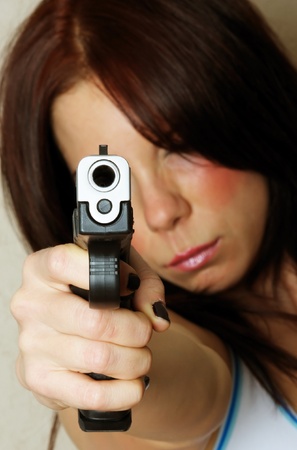 Close-up image of young attractive female pointing gun.  Focus is on barrel of gun.の写真素材