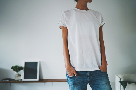 hipster tanned girl demonstrates a blank white T-shirt with an empty space for text or design. Horizontal mockup. Home interiorの写真素材