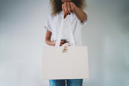 The hipster girl is holding a white paper bag with textile handles in her hand.の写真素材