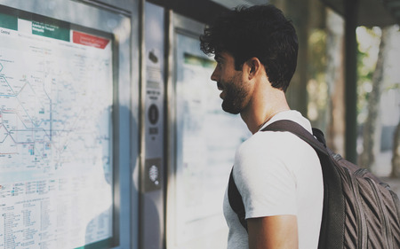 Young bearded international student searching the route on a public transportation system map in...