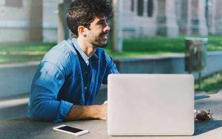 Successful freelancer thinking on a new project while sitting outdoors with a laptop and a smartphone.の写真素材