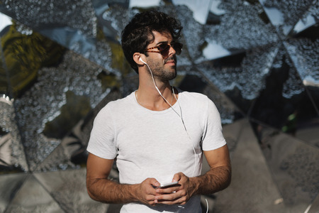 Young man wearing blank white t-shirt enjoys the music he listens on a mobile phone while walking outdoors in the morning.の写真素材