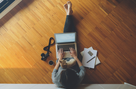 top view of a female freelance photographer working with laptop computer, sitting on a wooden floor with her little dog on her lap. girl looks at photos from vacation. Vintage camera.の写真素材