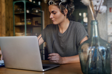 International student girl is working on the new project by chatting online by a portable computer connected to the public wi-fi network. Freelancer female is working on a laptop indoors.の写真素材