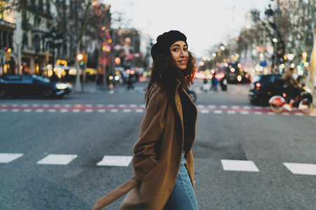 a young attractive girl crosses the road during a shopping stroll through the shopping street of the European city in a season of discounts against a background of blurry lights of the evening cityの写真素材