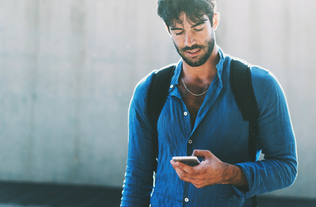 portrait of a young modern businessman who checks the e-mail on the smartphone on the way to a business meeting. beautiful guy typing a text message on the cell phone while walking on a city streetの写真素材