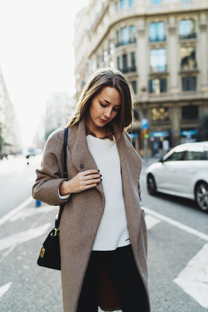 Portrait of a beautiful caucasian woman with long hair wearing stylish clothes walking down the street on a blurred urban background. Travel blogger in a trendy look standing outdoors.の写真素材