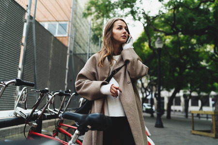 International student girl calling to bike rental support center to check the transaction information. Tourist female renting city bicycle in european city she visited for weekend journey.の写真素材