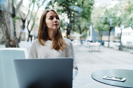 Young successful entrepreneur female reading business emails on a laptop connected to public wifi in a modern coffee shop. Hipster girl surfing the web on a laptop while enjoying free time.の写真素材