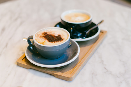 Two cups of cappuccino with cinnamon placed on a little table. Brunch coffee for couple in love. Two mugs of aromatic coffee to relax during coffee break. Delicious flavour of a natural coffee beans.の写真素材