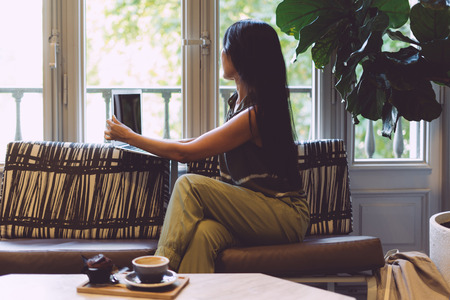 Modern asian woman is shopping online while sitting in a cafe with a laptop connected to the wi-fi. Fashion blogger is working on a new article by a portable computer while sitting in a coffee shop.の写真素材