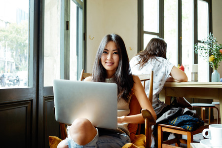 Casual asian young woman using laptop for distance job at coffee shop.portrait of an attractive girl who communicates online on her PCの写真素材