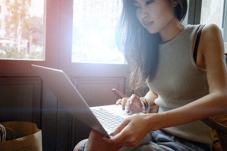 Attractive young Asian girl working at a coffee shop with a laptop.freelancer girl working at cafe via net-book.young woman writes a text message on laptop keyboardの写真素材