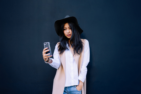 Asian young beautiful girl using her smart-phone Selfie on a black wall backgroundの写真素材