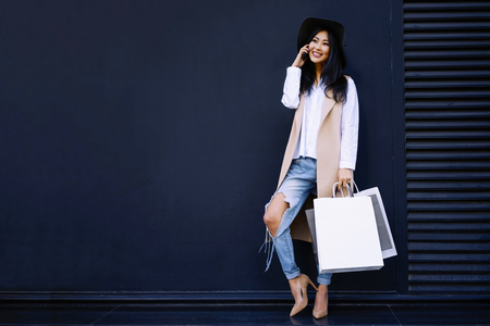 beautiful young Asian woman talking on the phone and holding white blank bags in her hand on the background of black wall with copy space for your text or design.の写真素材