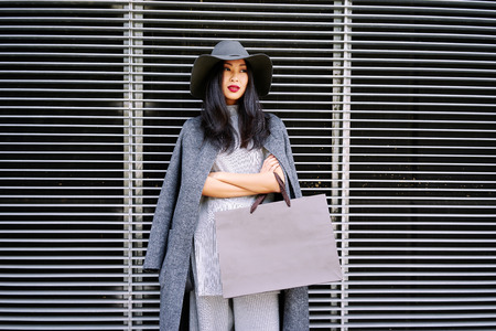 young beautiful well-dressed Asian girl posing and holding a blank paper bag with empty space for your text or logoの写真素材